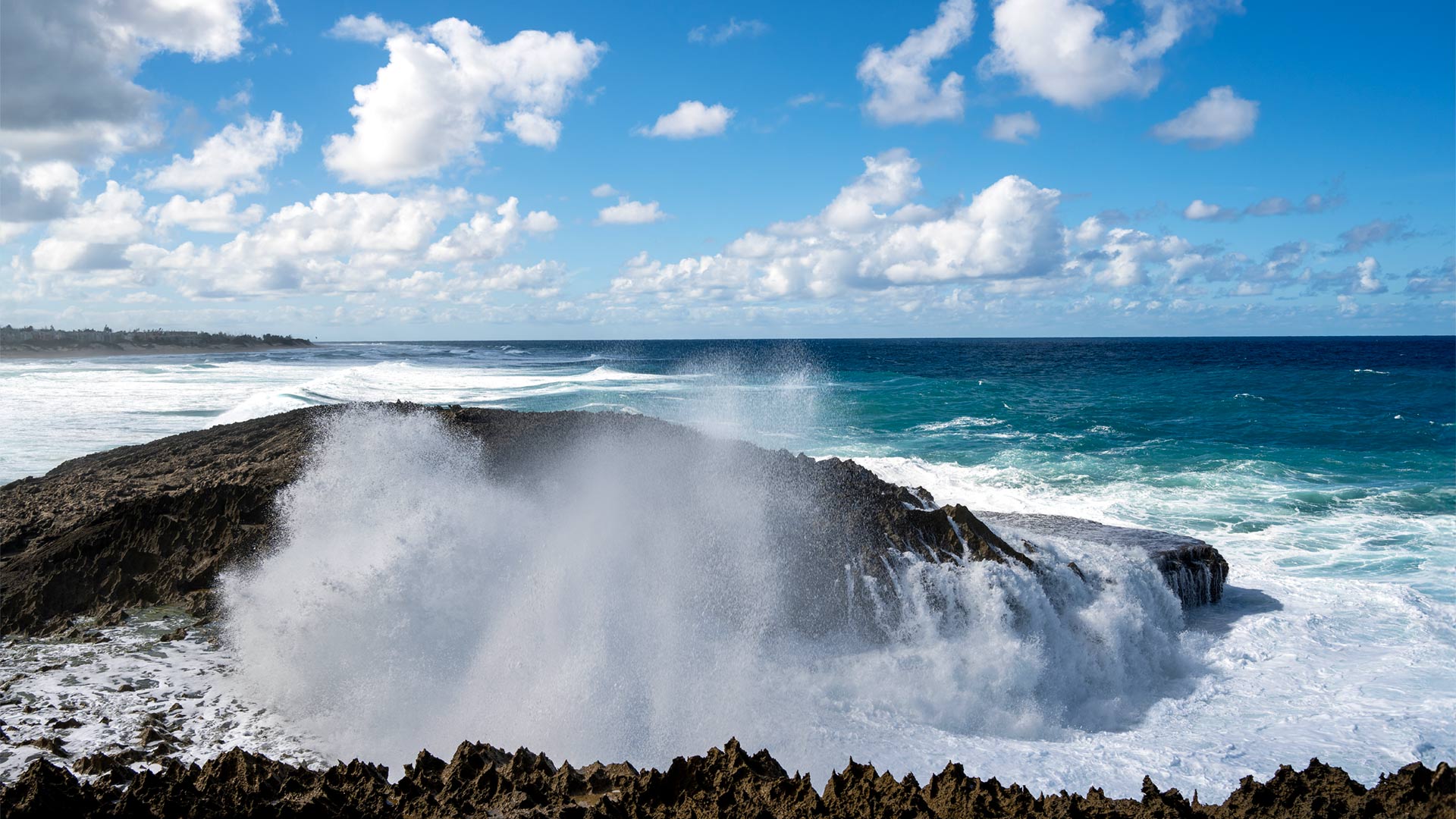 Powerful ocean waves crashing against dramatic rock formations on Puerto Rico’s north coast, captured under a bright blue sky.