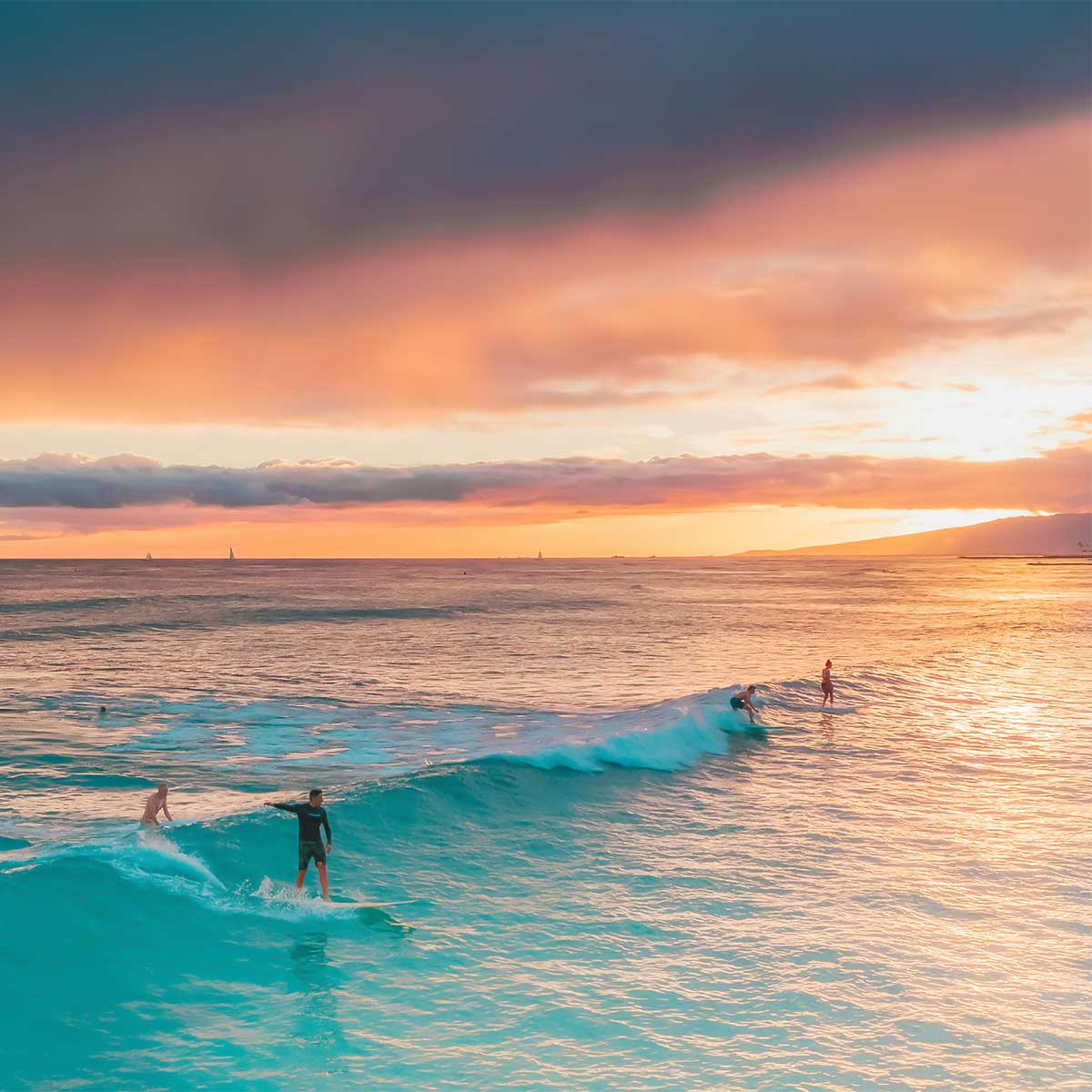 Surfers catching waves under a golden sky — evening energy and ocean glow.