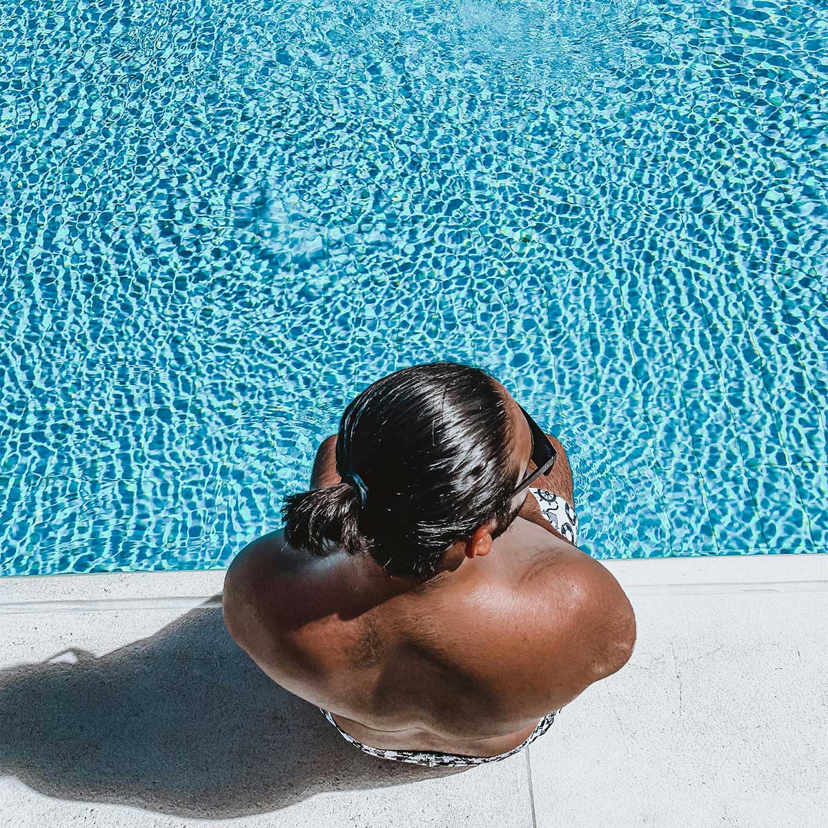 Man sitting at pool edge with sun reflecting on water — quiet island moment.