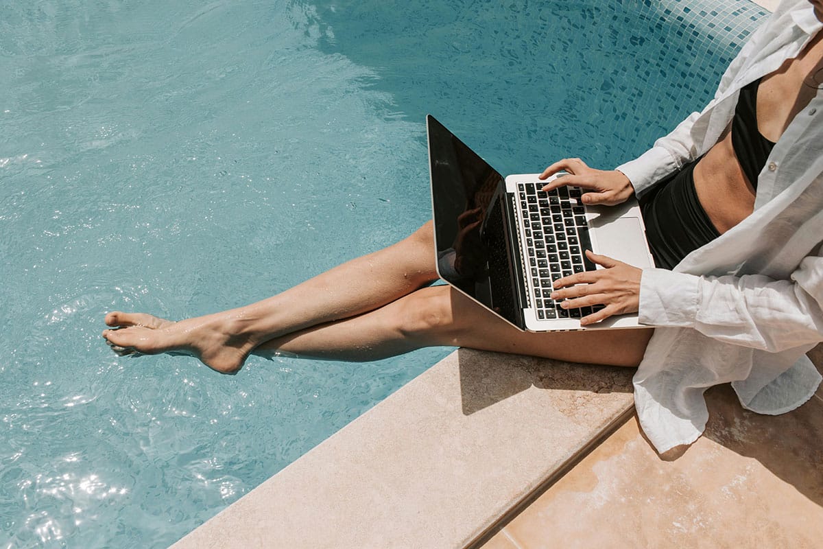 Airbnb host working on a laptop by the pool, showing the freedom of managing vacation rentals and bookings online.