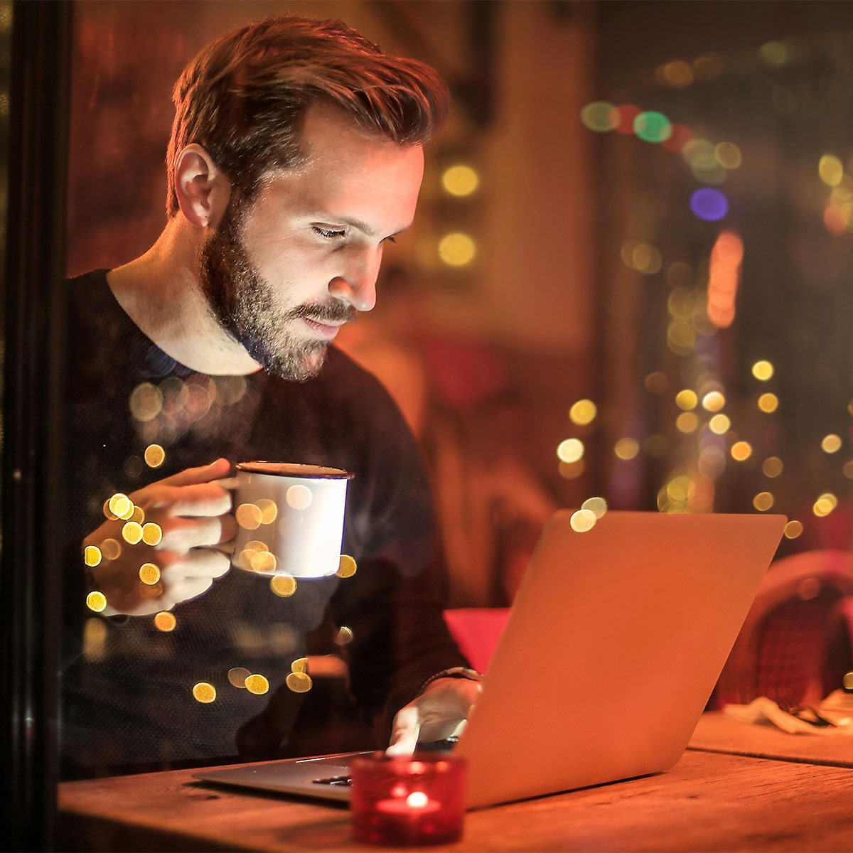 Man drinking coffee while browsing a small business website on a laptop in a cozy café.