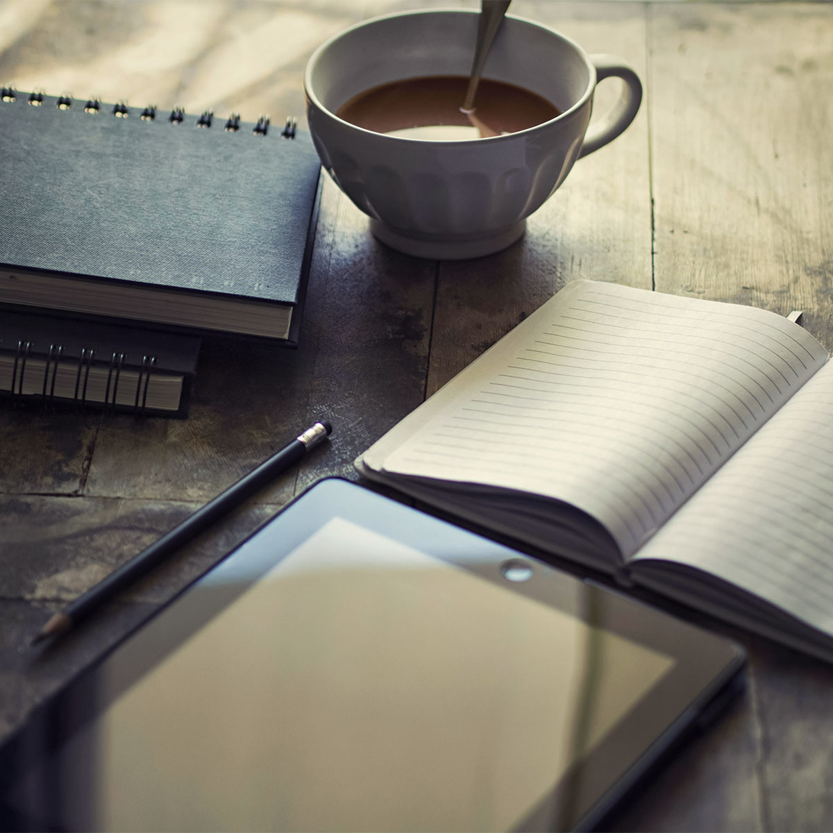 Open notebook, coffee cup, and tablet on a wooden desk representing Visible PR’s creative planning process.